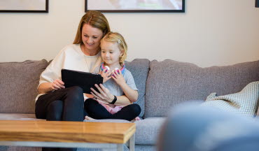 Mamma och dotter sitter i soffan och tittar på en padda tillsammans