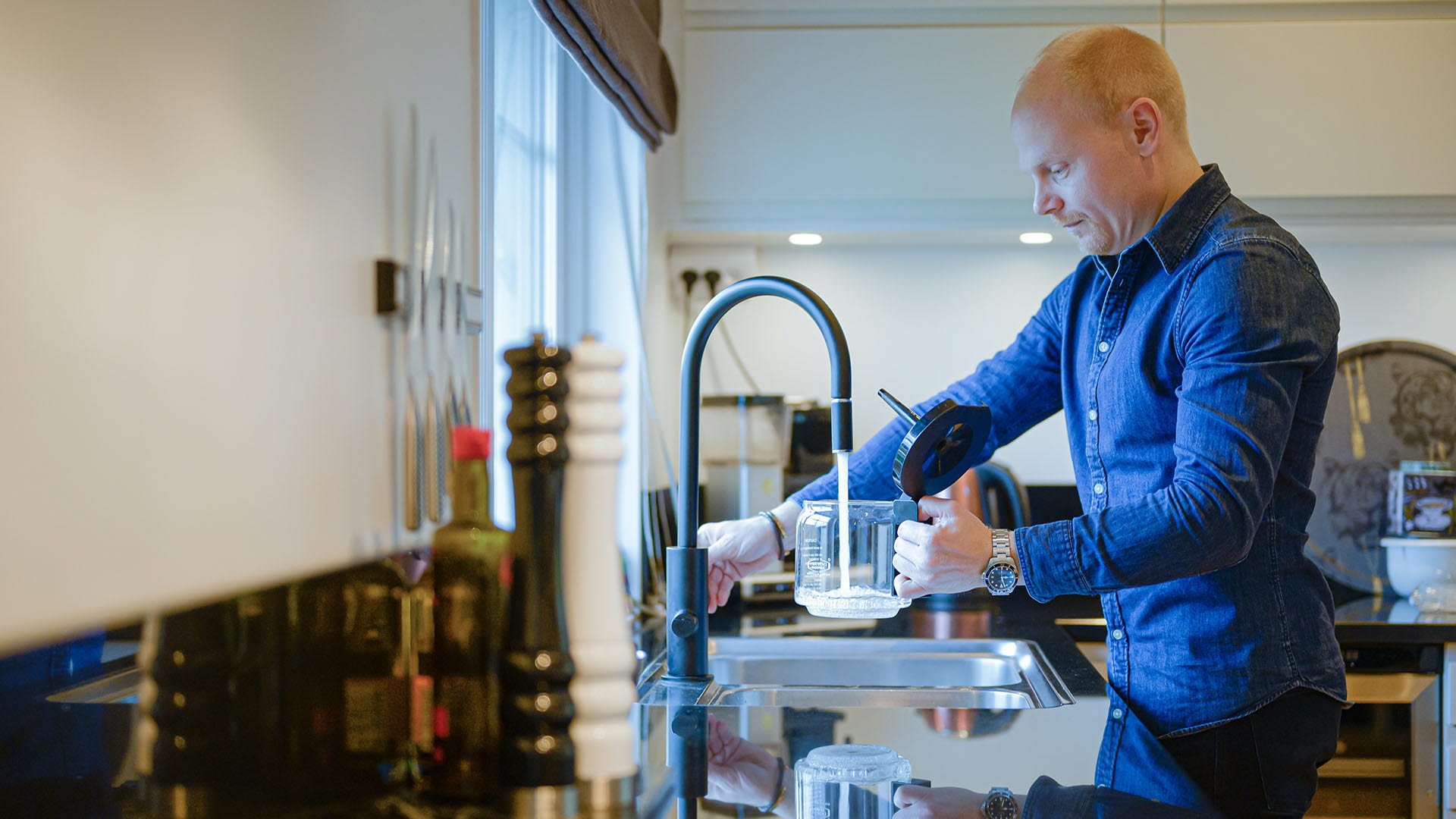 En man fyller på en vattenkanna i köket hemma