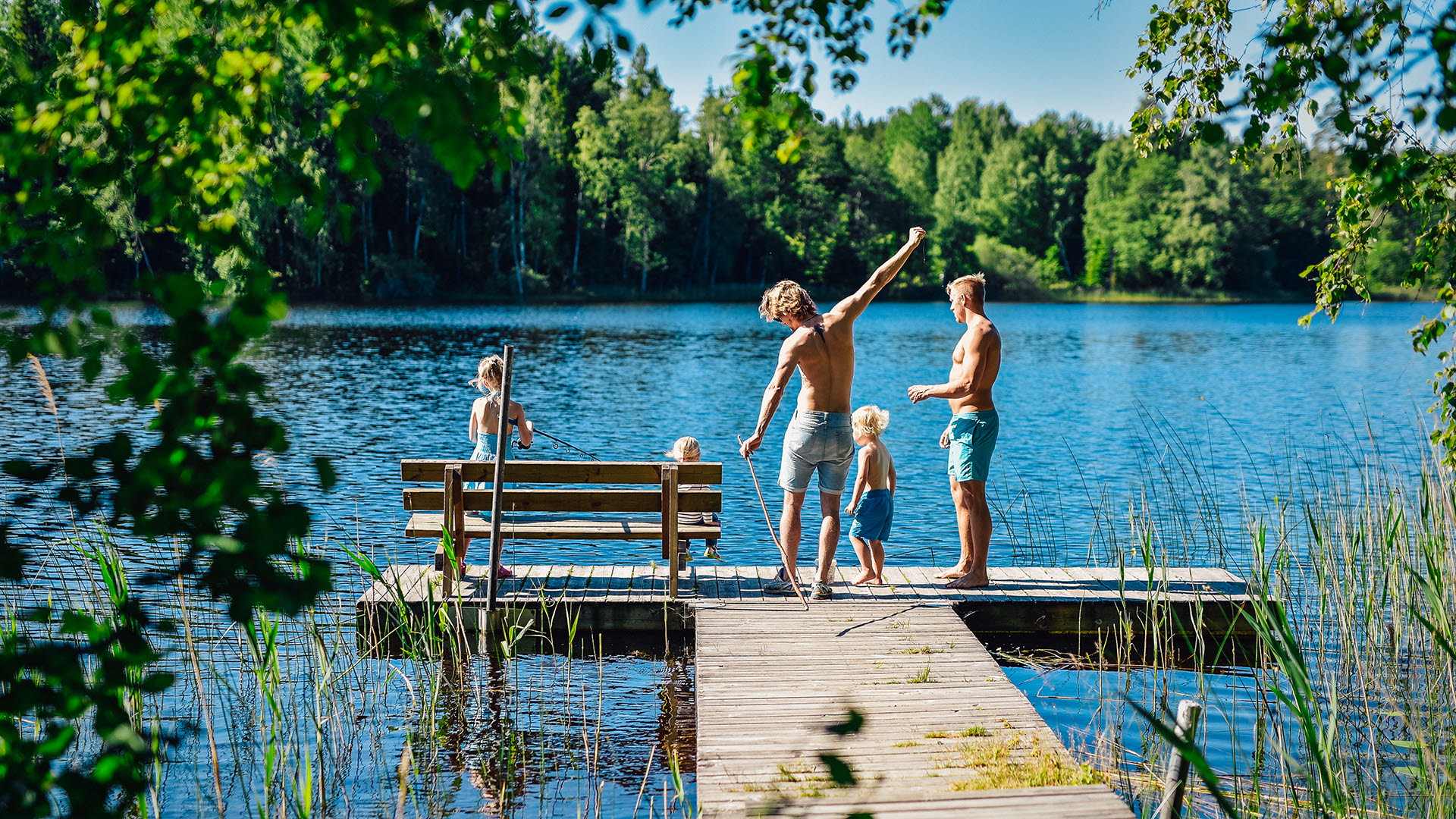 Tre barn och två vuxna står på en badbrygga vid svensk sjö