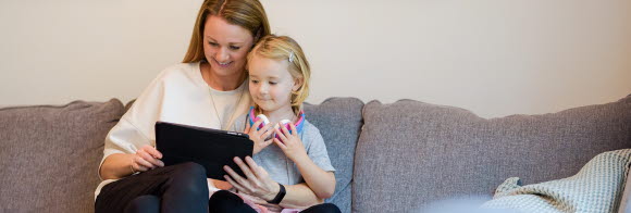 Mamma och dotter sitter i soffan och tittar på en padda tillsammans