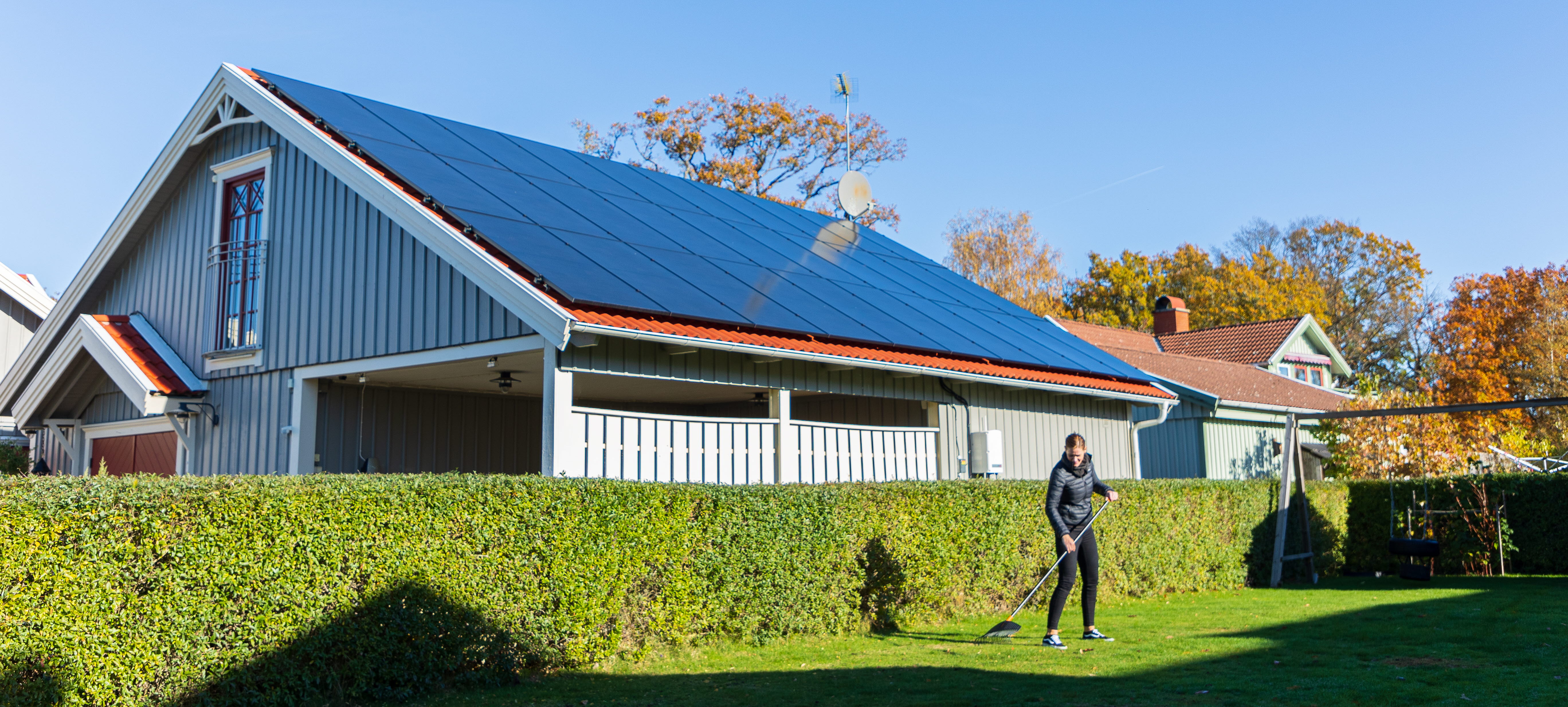 Villa med solceller på taket med en person som krattar framför