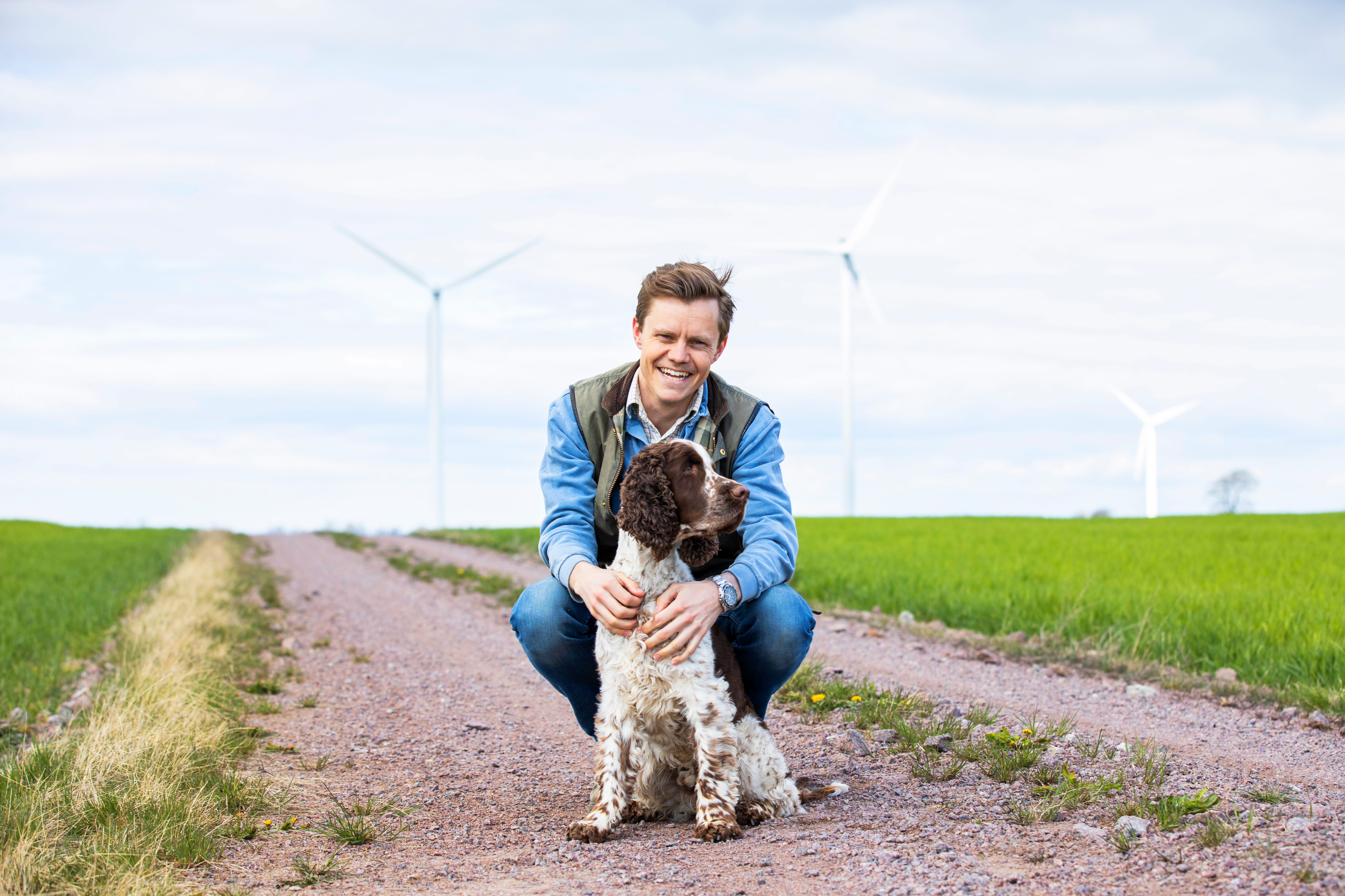 Man med hund framför vindkraftverk (foto)