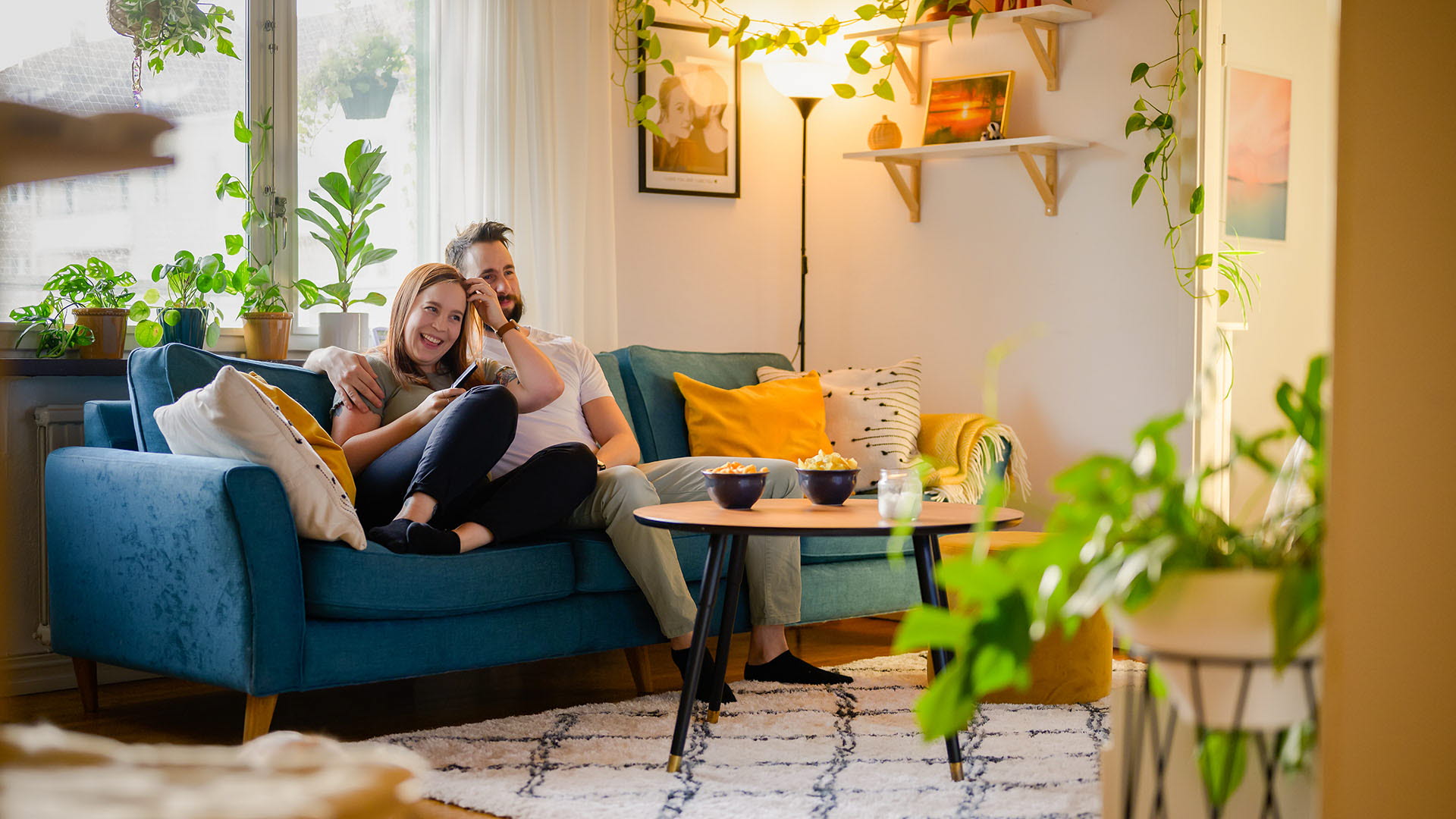 Ett par sitter uppkrupna i soffan och tittar på tv