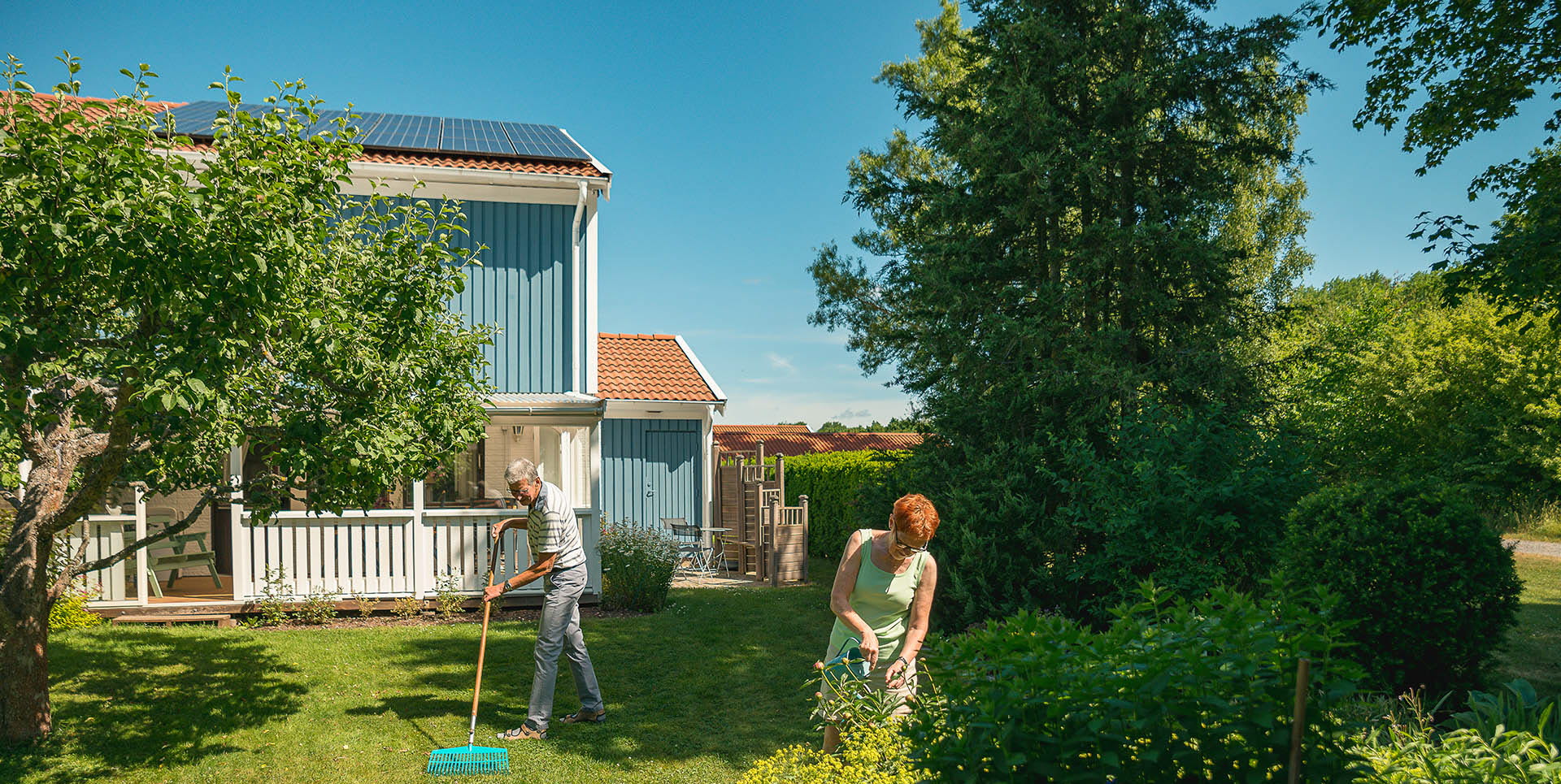 Äldre par arbetar i trädgården. På hustaket syns solceller.