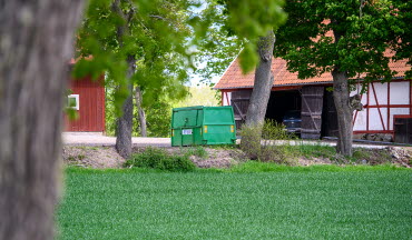 Hyrd grön container står på gårdsplan på landsbygden